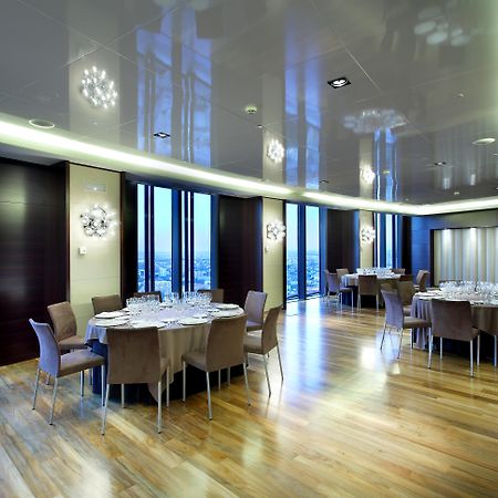Eurostars Madrid Tower Hotell Exteriör bild The photo depicts a modern dining room or banquet hall with large windows that provide a view of the outside. The room features elegant wooden flooring and contemporary furniture, including round tables set with plates, glasses, and cutlery. Various 