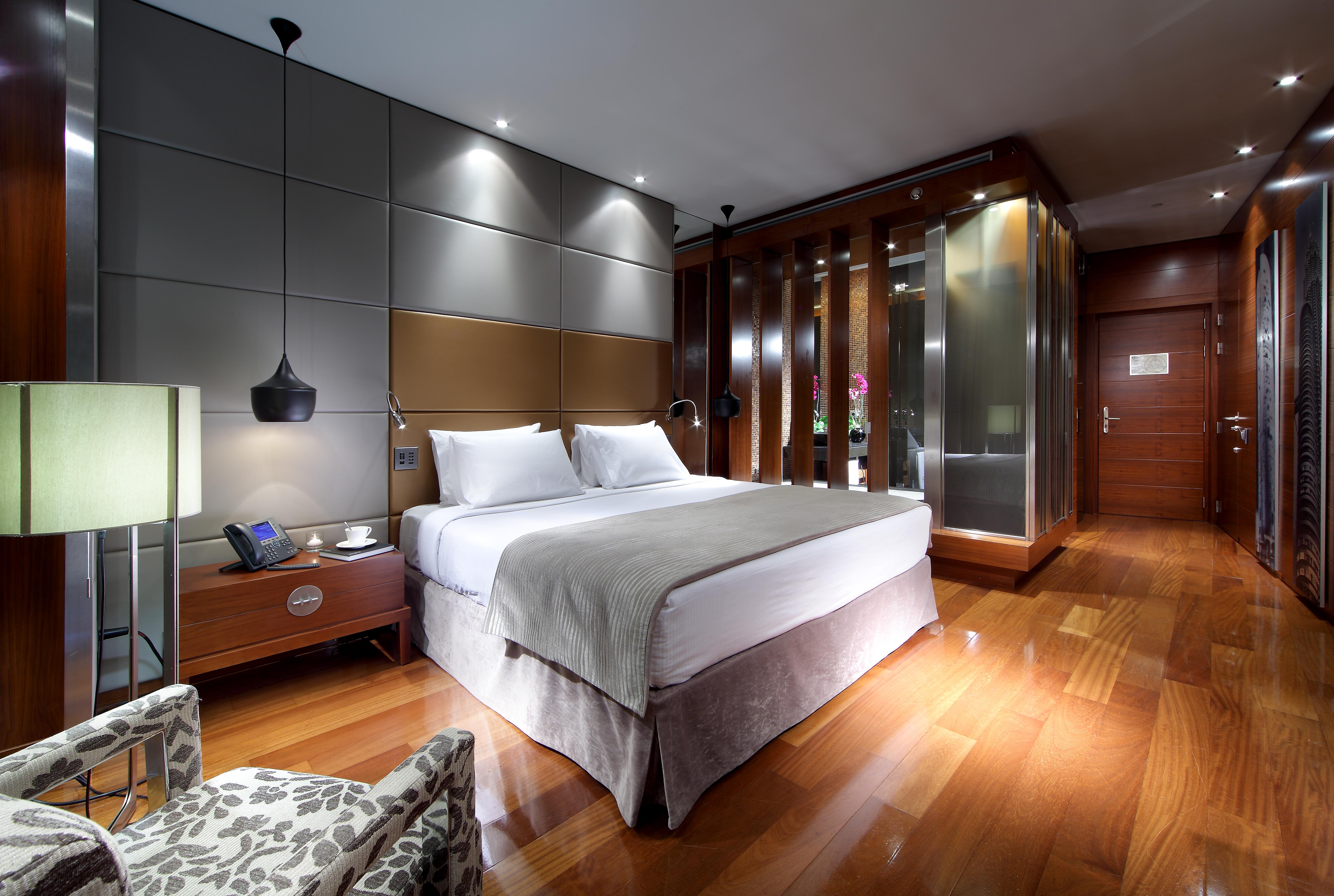 Eurostars Madrid Tower Hotell Exteriör bild The photo shows a modern hotel room featuring a double bed dressed in white linens with a light gray blanket. Beside the bed, there is a stylish nightstand with a lamp and a phone. The room has a sleek design with wooden flooring and contemporary dec