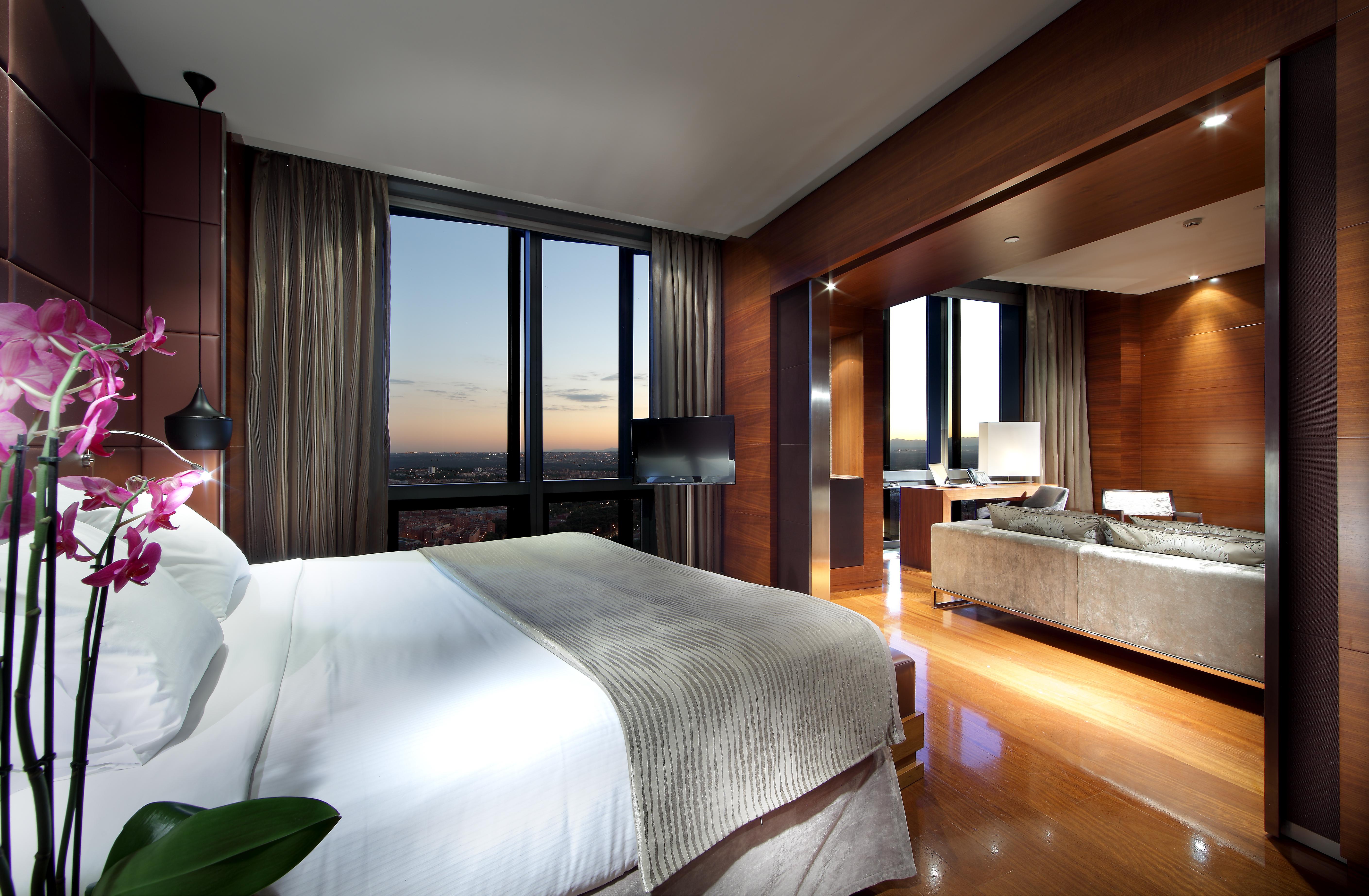 Eurostars Madrid Tower Hotell Exteriör bild The photo depicts a modern hotel room interior. It features a spacious layout with a large bed dressed in white linens, accompanied by a subtle patterned blanket. To the side, there is a small decorative plant. 

The room is illuminated by ambient li