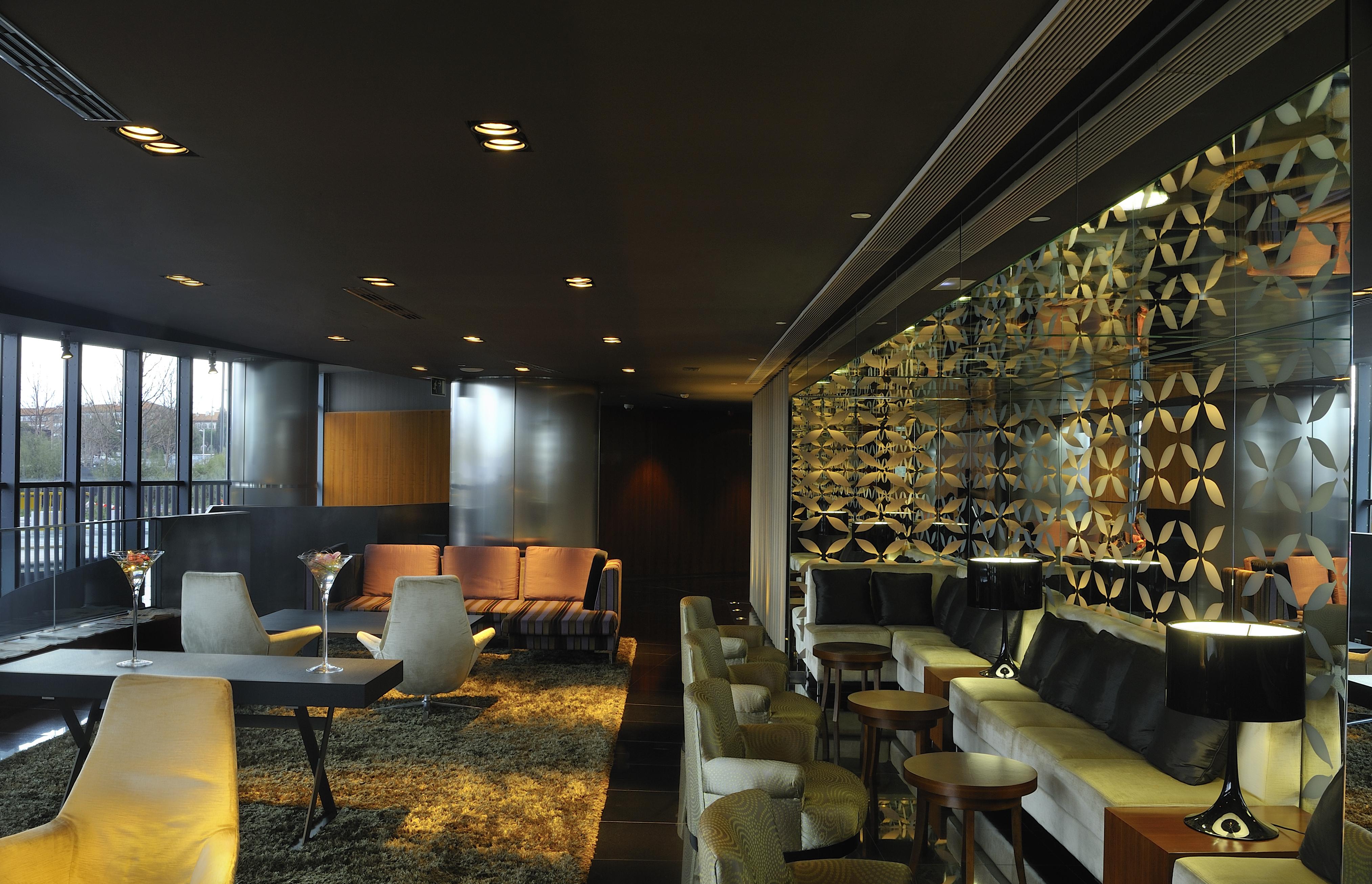 Eurostars Madrid Tower Hotell Exteriör bild The photo shows a contemporary and stylish interior space, likely a lounge or bar. The design features a mix of seating arrangements, including plush chairs and modern sofas, set against a dark backdrop with soft lighting. A decorative wall with an i