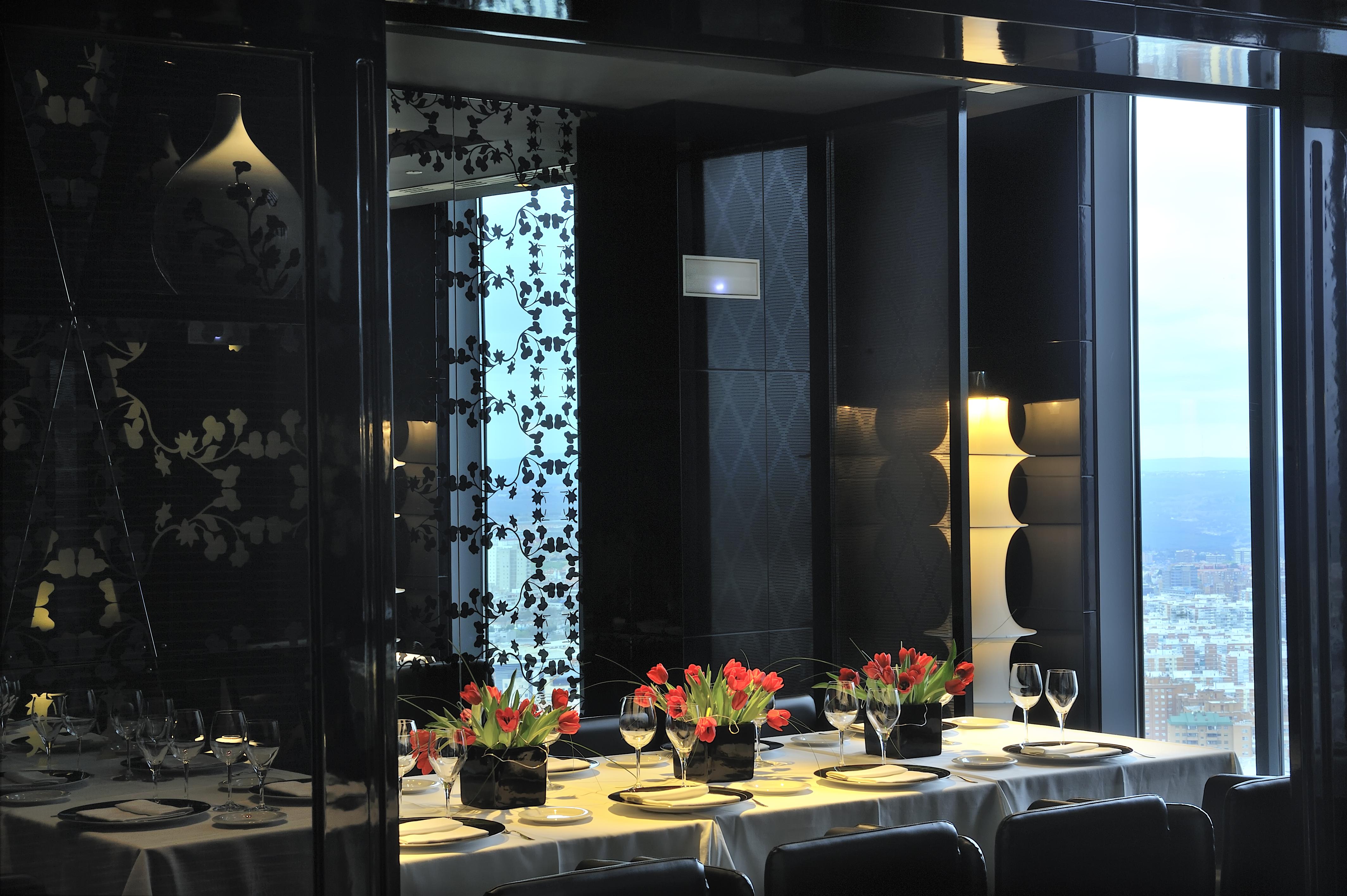 Eurostars Madrid Tower Hotell Exteriör bild The photo shows a stylishly decorated dining area with a long table set for a meal. The table is adorned with elegant plates, glasses, and small vases of vibrant tulips as centerpieces. The interior design features a mix of dark and light elements, w