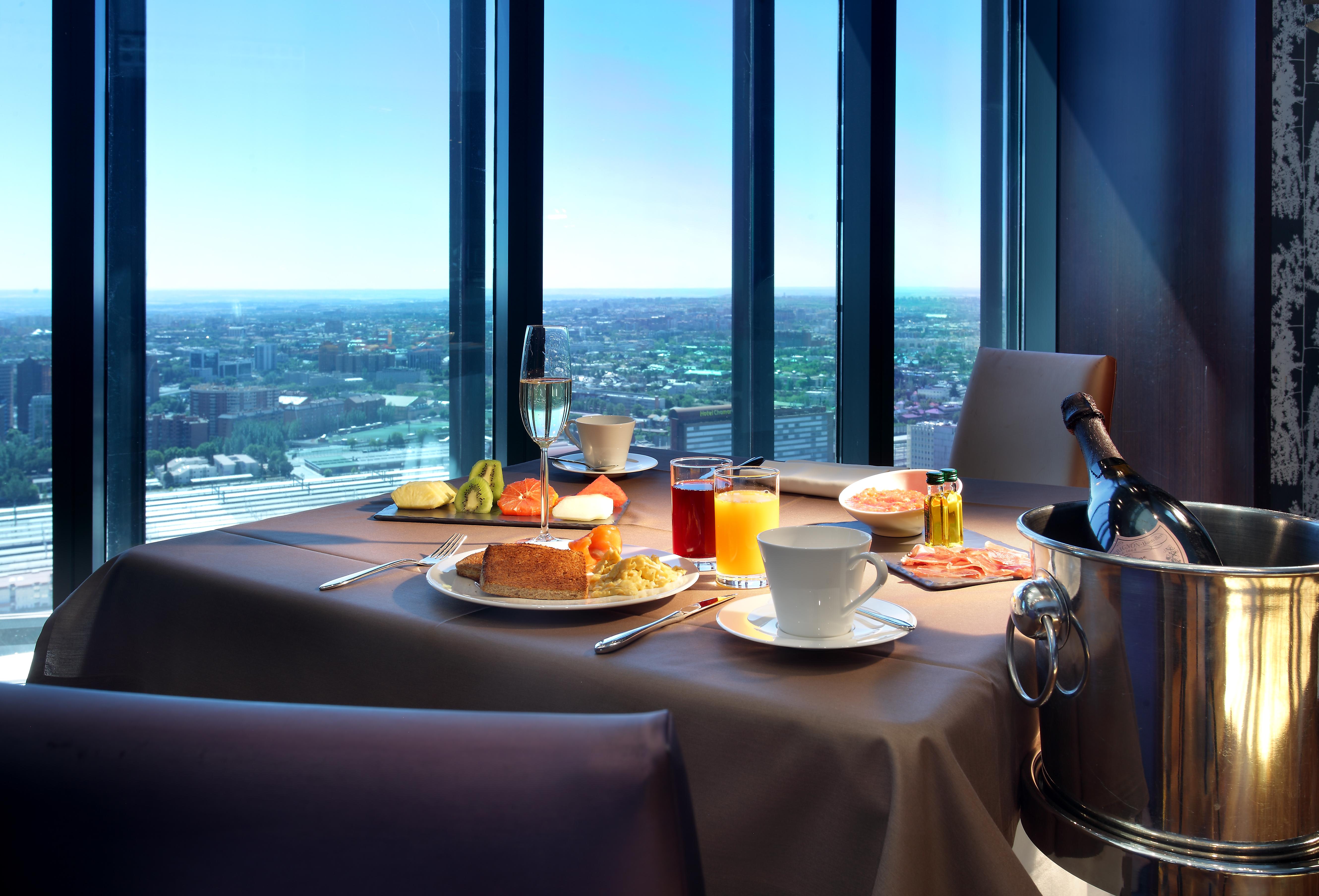 Eurostars Madrid Tower Hotell Exteriör bild The photo shows a beautifully set table with a scenic view through large windows. On the table, there are various food items, including a breakfast plate with items like eggs, pastries, and fruit. There are drinks, including a cup of coffee, a glass 