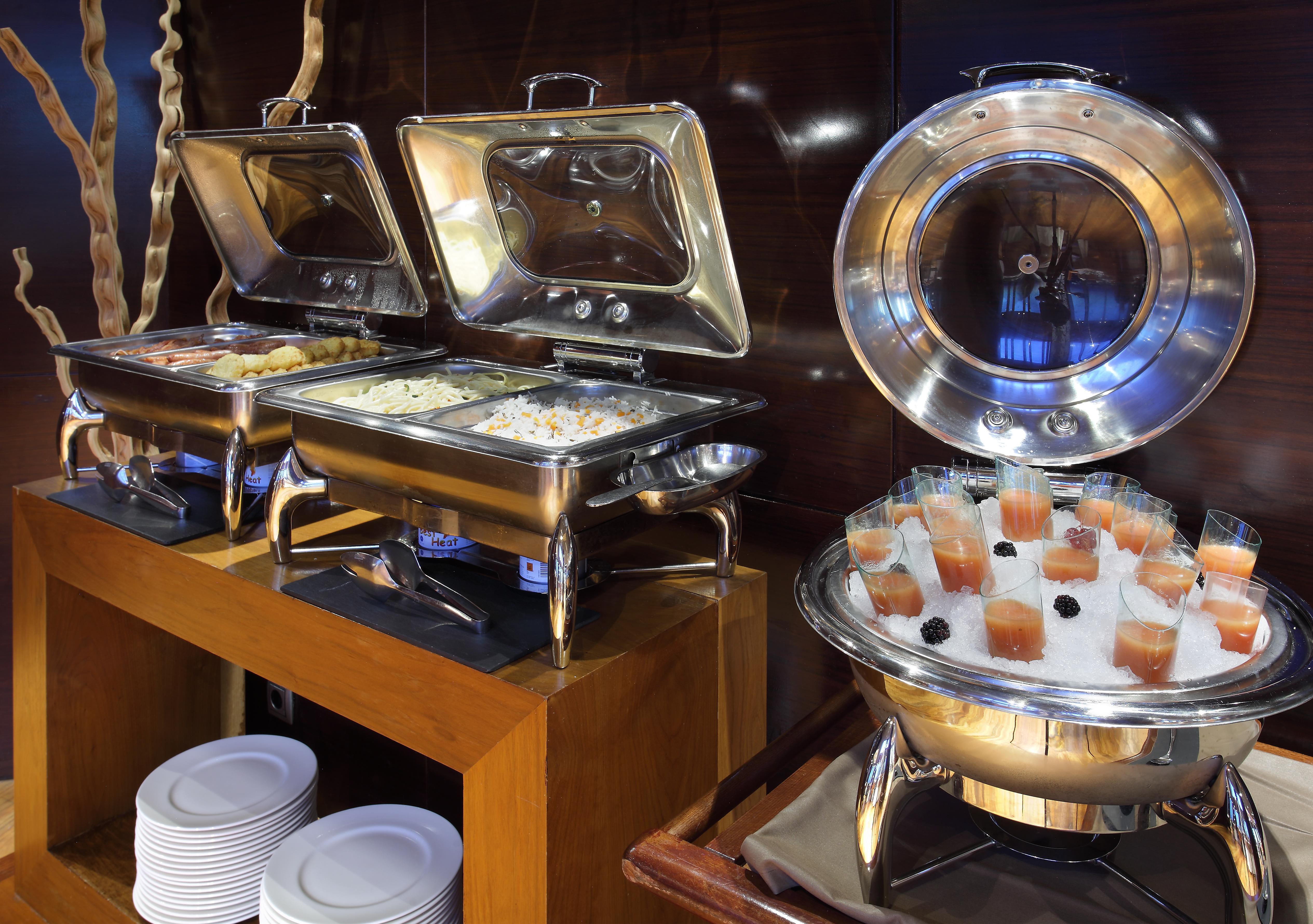 Eurostars Madrid Tower Hotell Exteriör bild The photo shows a buffet setup with several food items. On the left, there are two stainless steel chafing dishes, each containing food, possibly rice or a similar dish. On the right, there is a round chafing dish that holds small cups or glasses fil
