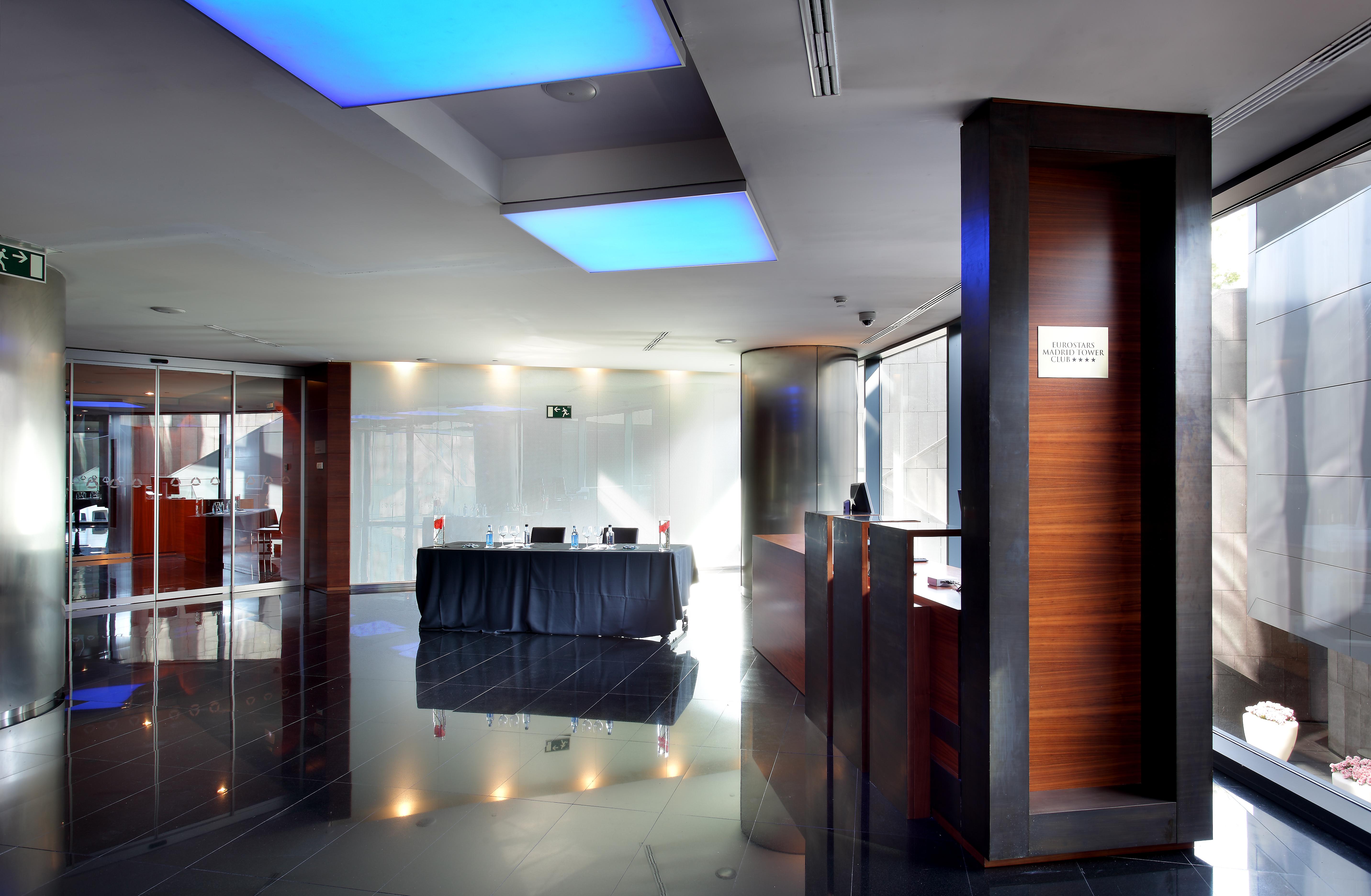 Eurostars Madrid Tower Hotell Exteriör bild The image shows the interior of a modern reception area. The space features sleek design elements, including glossy black flooring and walls. There is a front desk made of wood, which includes a sign, likely indicating reception services. Soft blue l