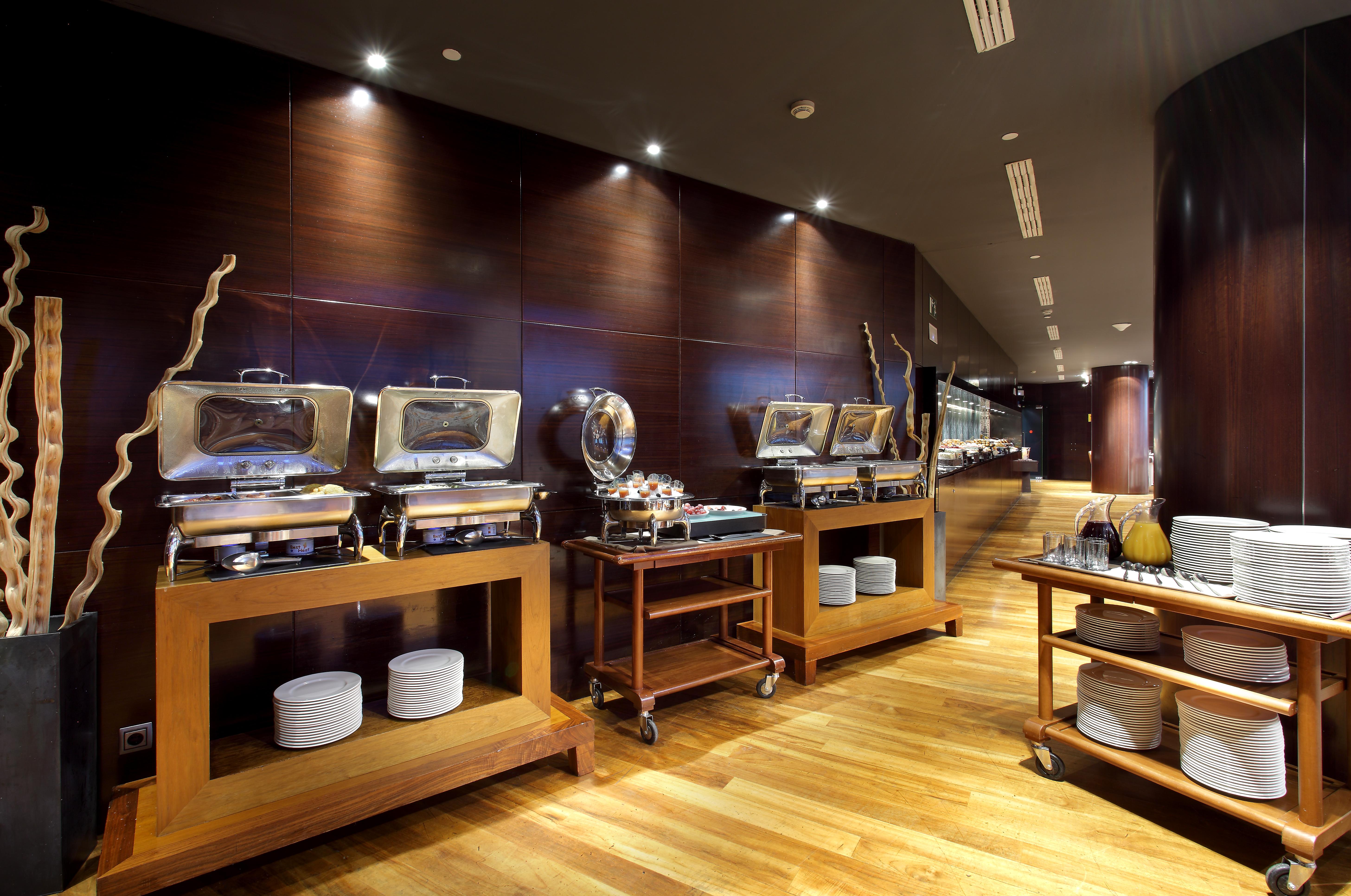 Eurostars Madrid Tower Hotell Exteriör bild The photo shows a modern restaurant buffet setting. There are several food warmers placed on wooden tables, showcasing a variety of dishes. The walls have a dark wood finish, and the lighting is soft and ambient, creating an elegant atmosphere. In fr