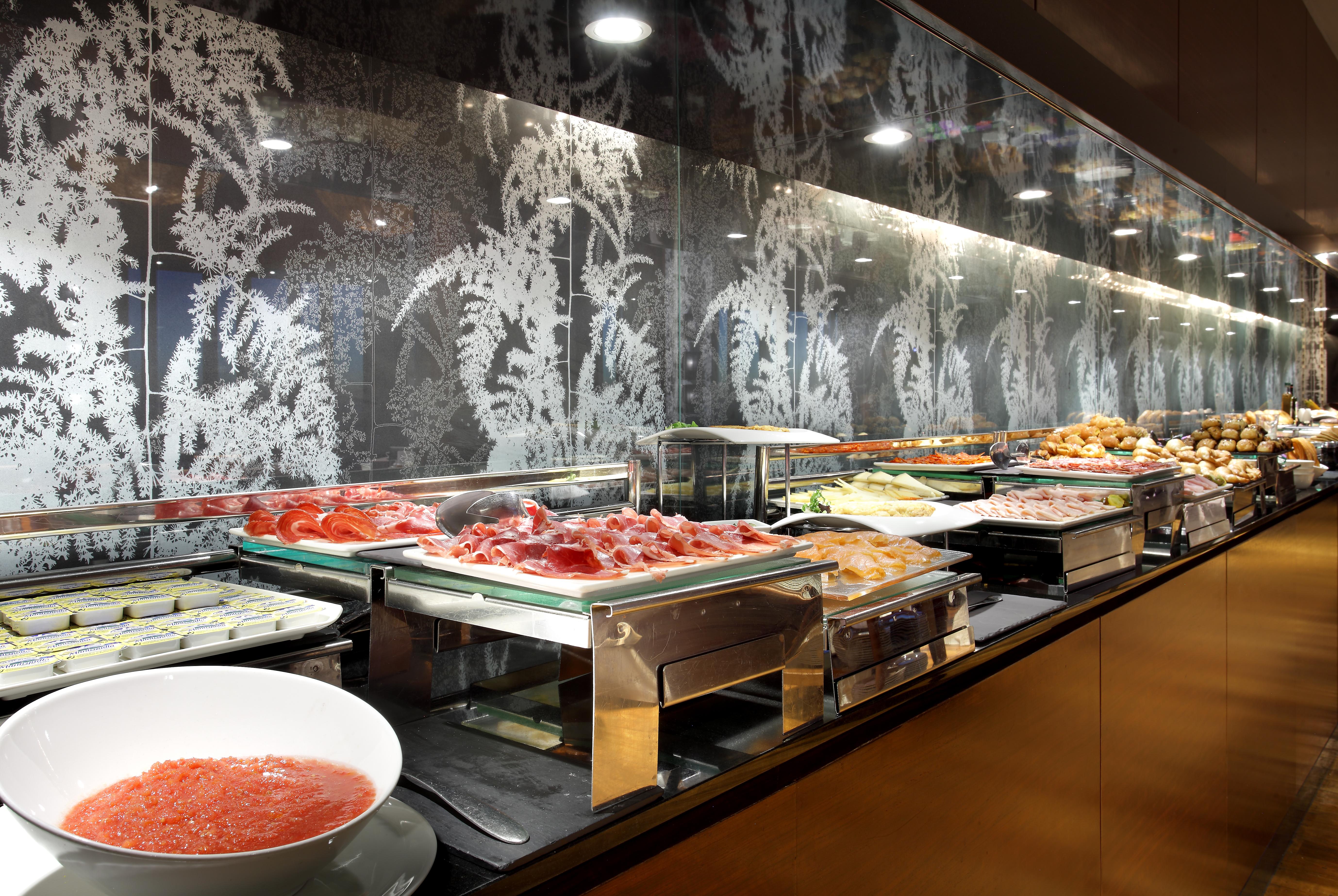 Eurostars Madrid Tower Hotell Exteriör bild The photo shows a buffet setup featuring a variety of food items. There are multiple trays and containers displaying an assortment of dishes, including salads, meats, and other prepared foods. A large bowl of sauce or dressing is also visible in fron