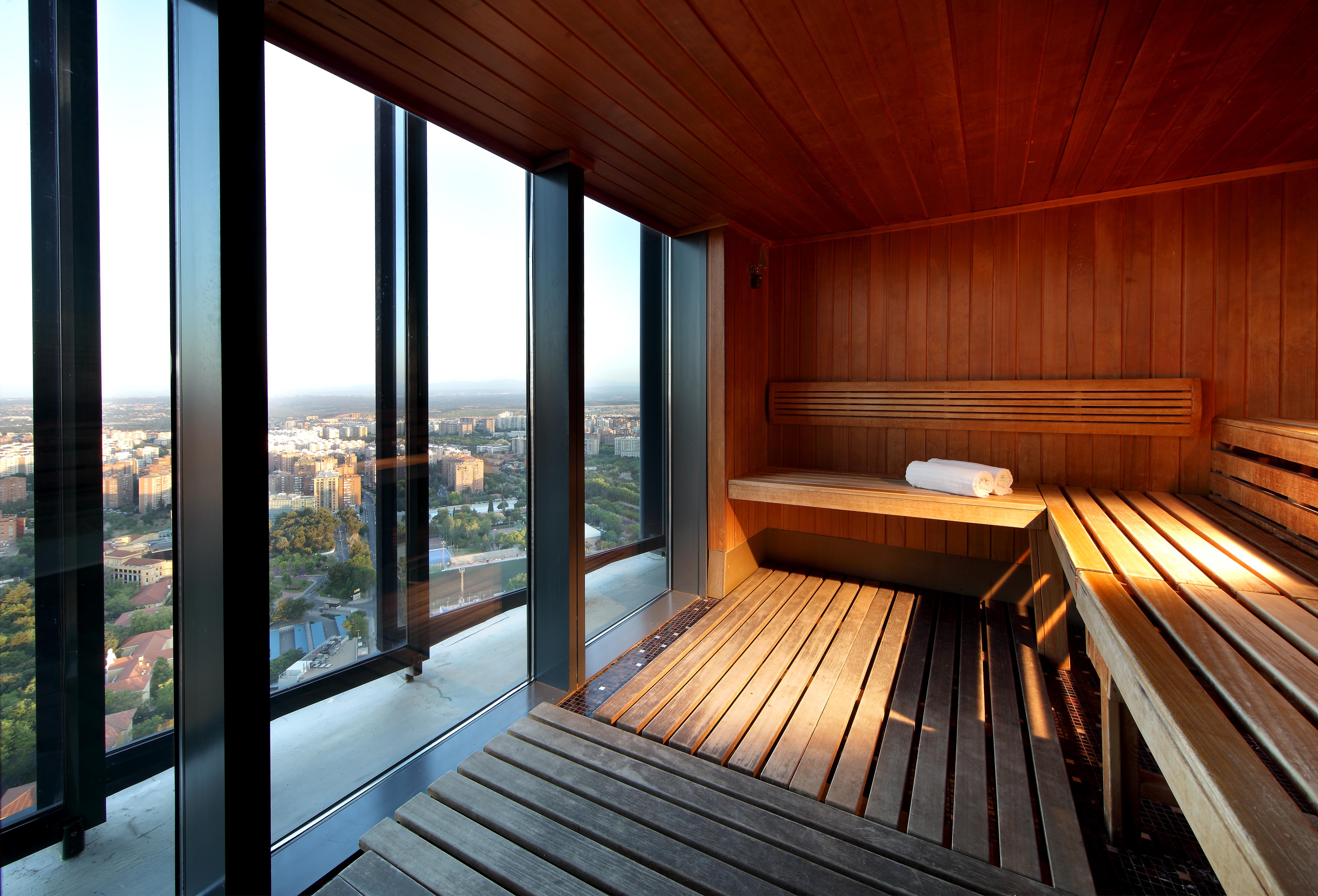 Eurostars Madrid Tower Hotell Exteriör bild The image shows a modern sauna with wooden interiors. The sauna features benches made of wood, providing a relaxing space. One of the benches has a rolled towel resting on it. Large glass windows allow for a panoramic view of the outside, showcasing 