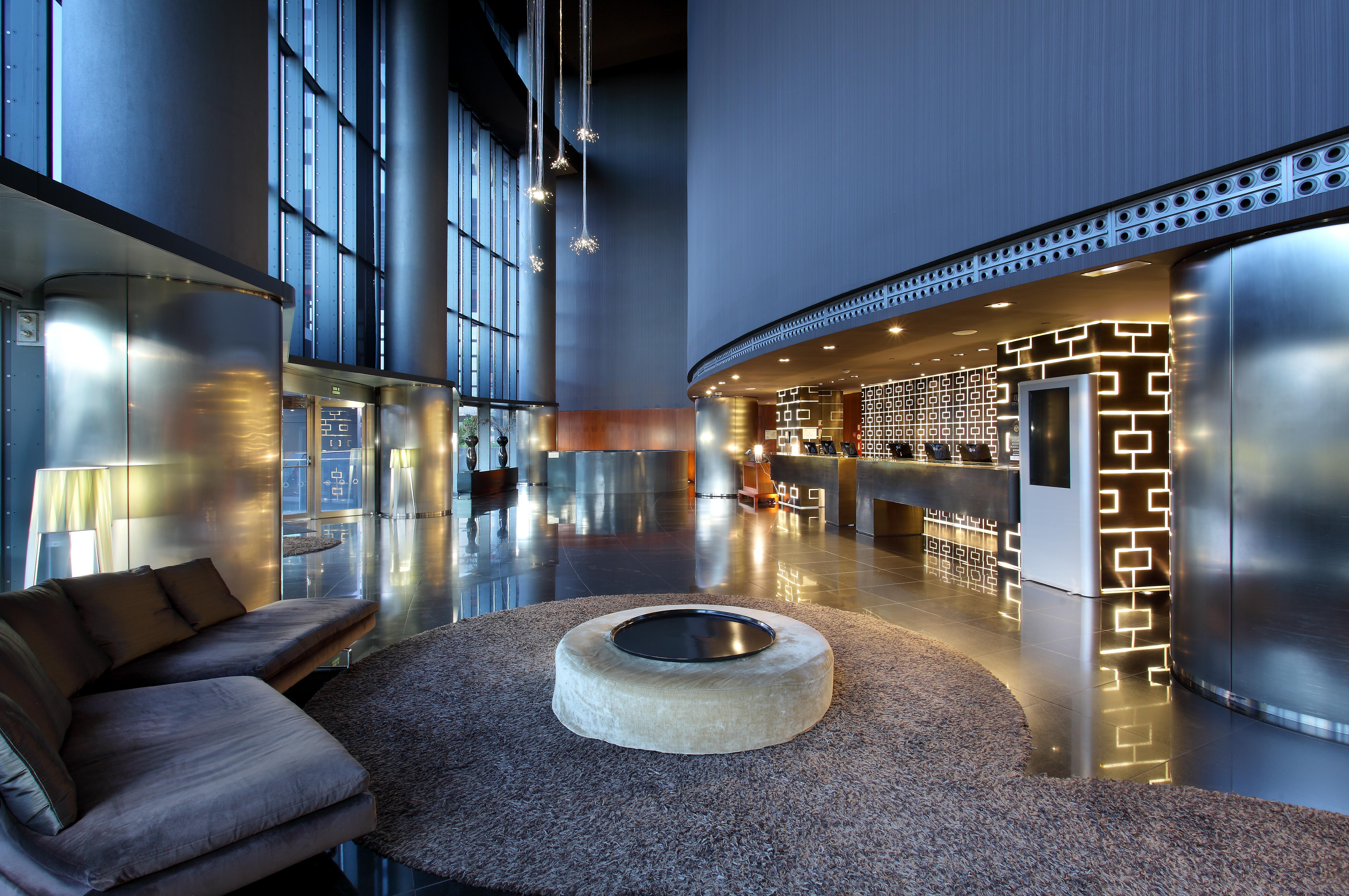 Eurostars Madrid Tower Hotell Exteriör bild The photo shows a modern hotel lobby with a sleek and sophisticated design. There is a large, open space featuring tall glass windows allowing natural light to flood in. The reception desk is stylishly designed, with a decorative wall behind it that 