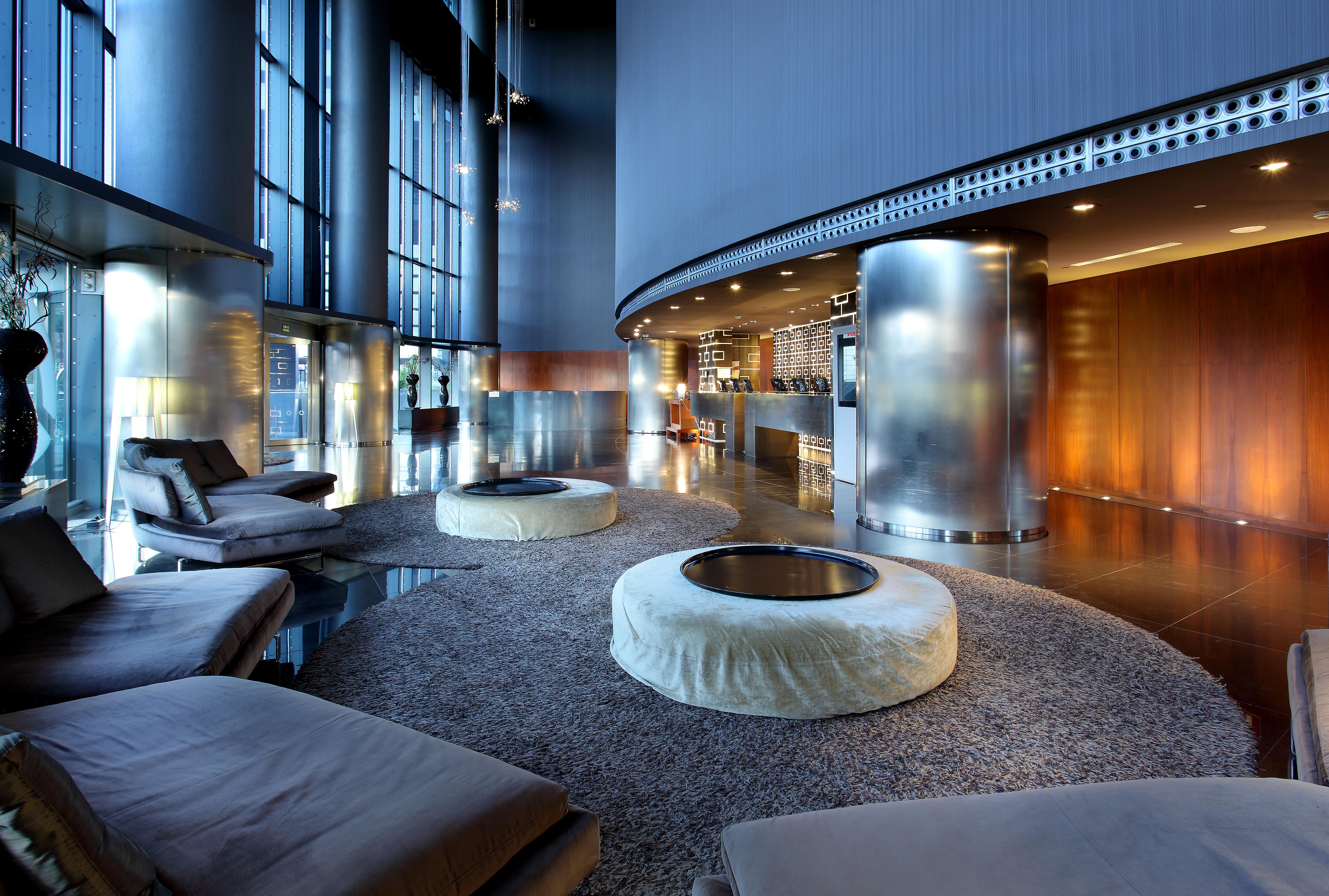 Eurostars Madrid Tower Hotell Exteriör bild The photo depicts a modern and stylish lounge area. The space features light-filled windows that allow for ample natural light, creating an airy atmosphere. There are several circular seating arrangements with plush, low-slung cushions arranged aroun
