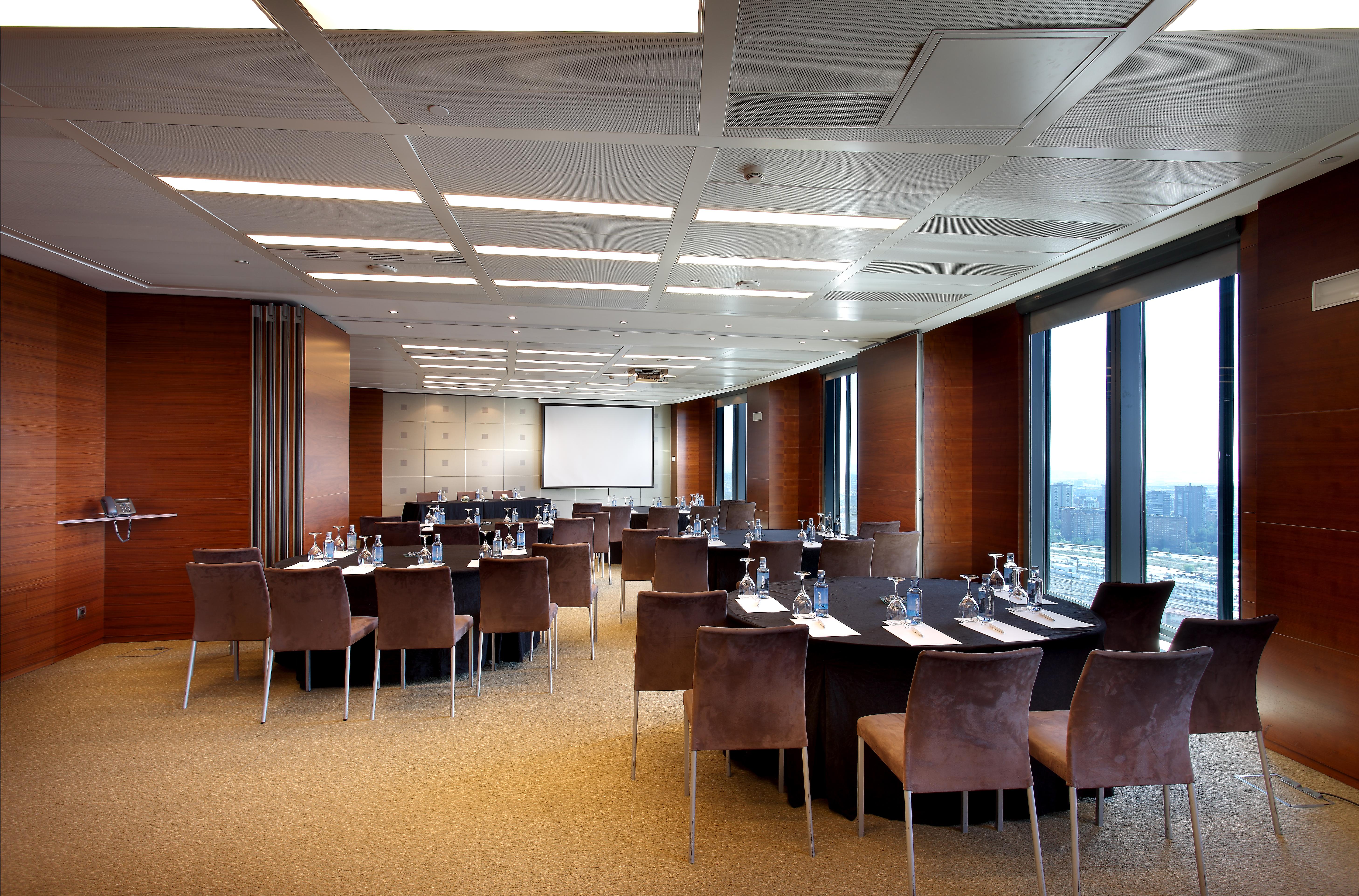 Eurostars Madrid Tower Hotell Exteriör bild The photo shows a modern conference room set up for a meeting or event. The room features a large, rectangular table surrounded by upholstered chairs. Each place at the table has a notepad and pen, and there are glasses of water provided. Large windo
