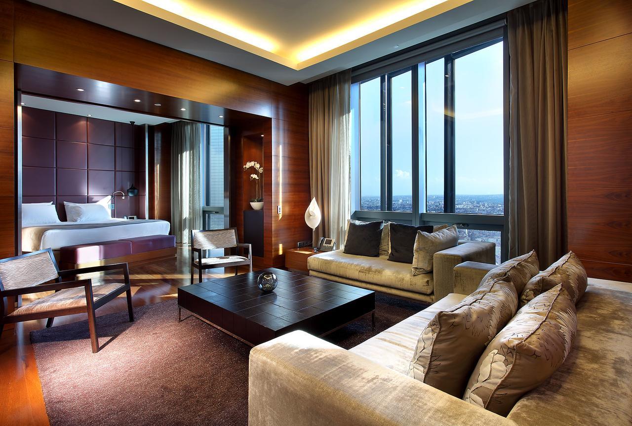 Eurostars Madrid Tower Hotell Exteriör bild The photo depicts a modern hotel room featuring a well-furnished living area and a bedroom space. The room has large windows that allow natural light to fill the space, providing a view of the city. The living area includes a plush sofa with decorati