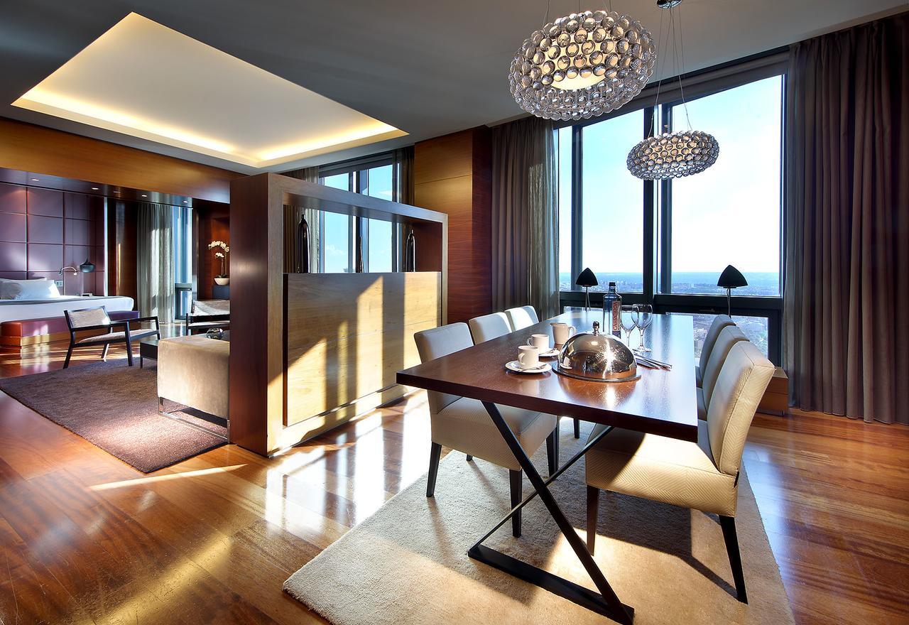 Eurostars Madrid Tower Hotell Exteriör bild The photo shows a modern dining area within a spacious interior. A sleek wooden dining table is set for a meal, featuring white dining chairs. Above the table, there are stylish chandelier lights illuminating the space. Large floor-to-ceiling windows
