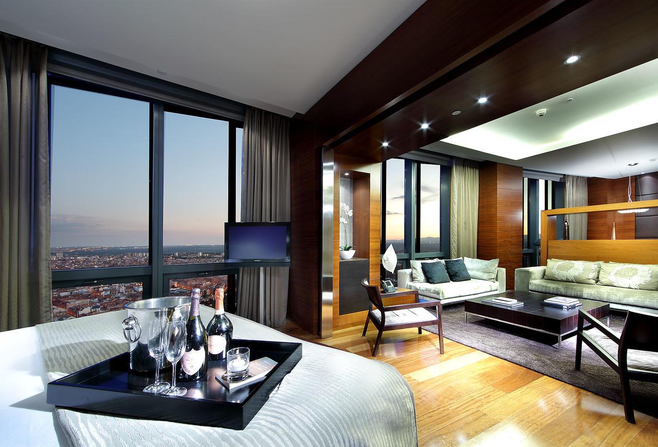 Eurostars Madrid Tower Hotell Exteriör bild The photo shows a luxurious hotel suite with modern decor. On one side, there is a bedroom area featuring a large bed, while on the other side, there is a spacious living area with a comfortable sofa and coffee table. The room is well-lit with stylis