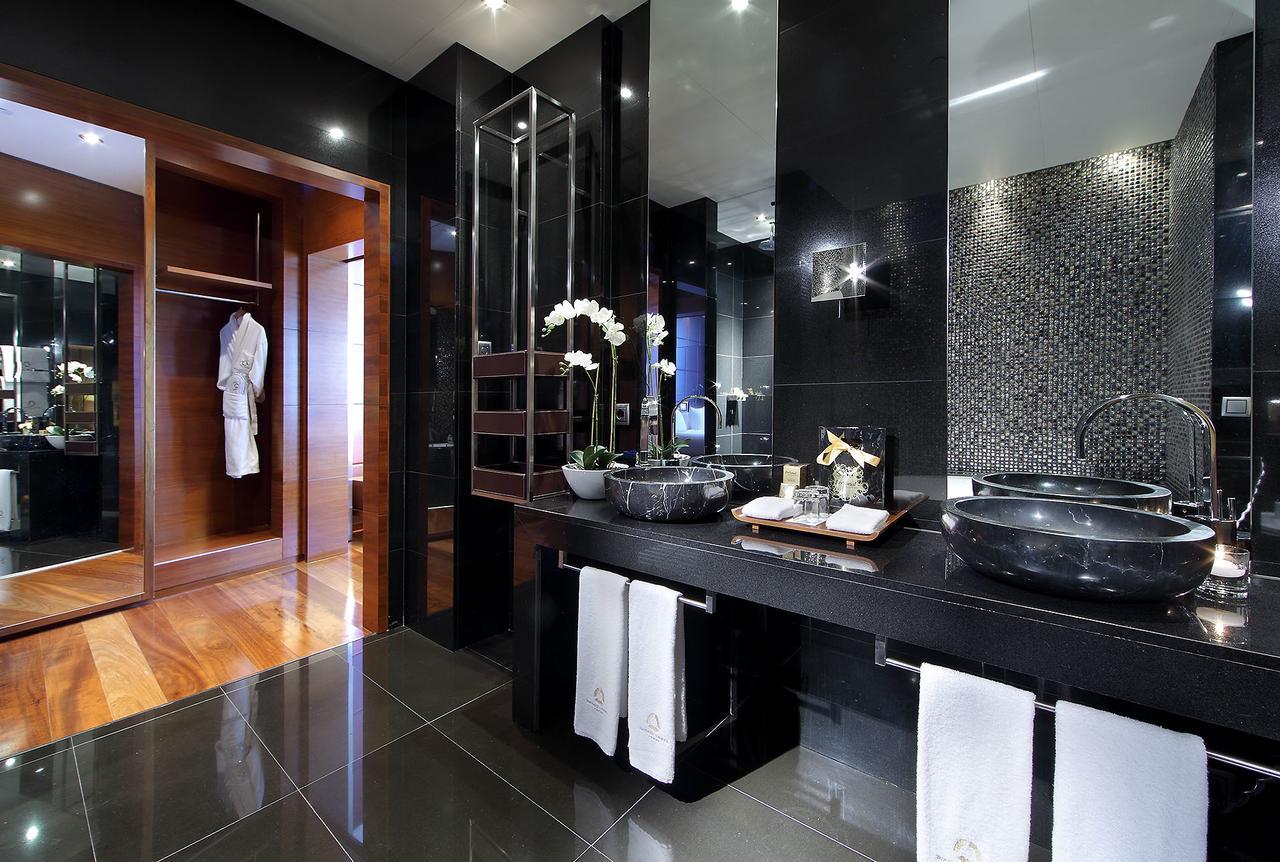 Eurostars Madrid Tower Hotell Exteriör bild The photo shows a modern and elegant bathroom with a contemporary design. It features dual black stone sinks with sleek faucets positioned on a dark countertop. The walls are adorned with shiny black tiles and a mosaic pattern, contributing to a luxu