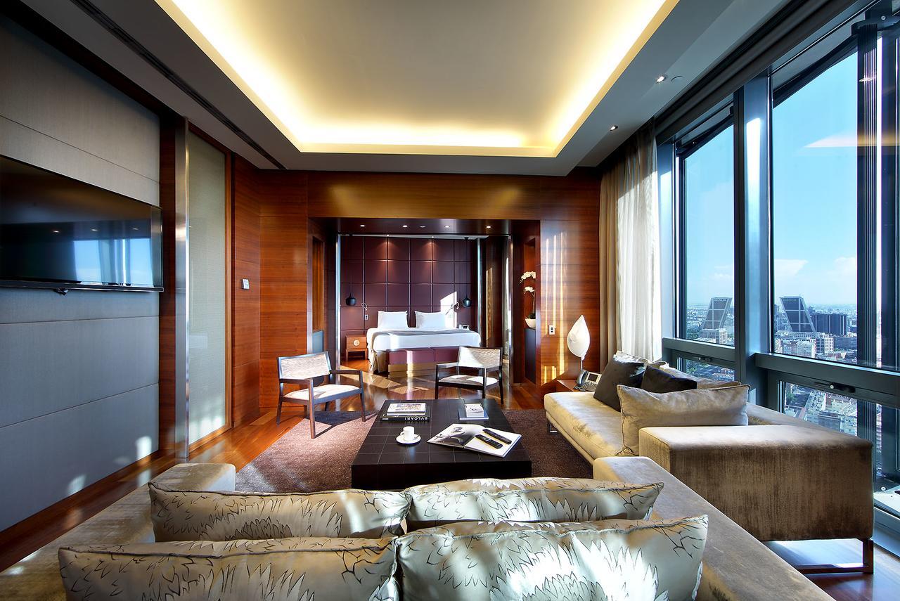 Eurostars Madrid Tower Hotell Exteriör bild The photo shows a luxurious hotel room or suite with a modern design. It features large windows that offer a view of the outside, letting in plenty of natural light. The interior has warm wooden accents on the walls and sophisticated lighting through