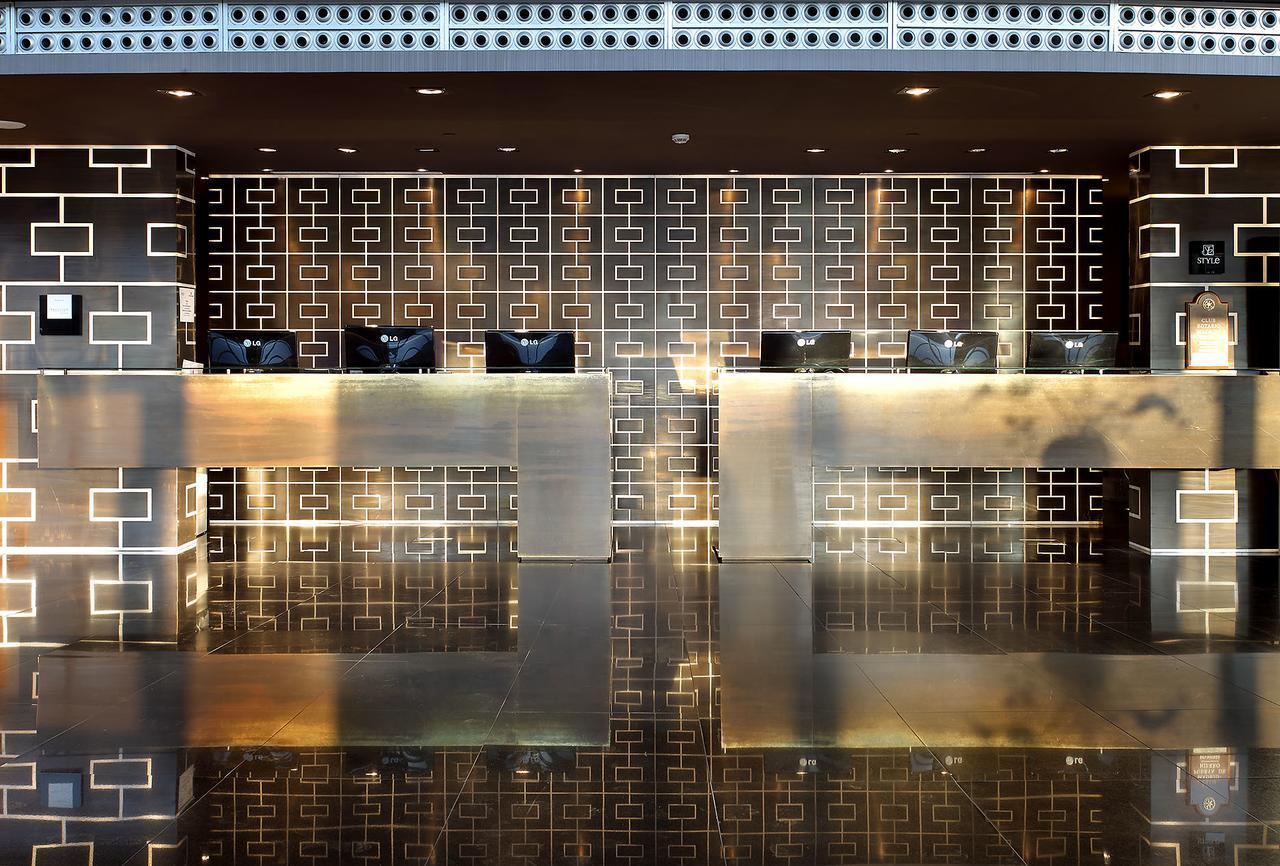 Eurostars Madrid Tower Hotell Exteriör bild The photo shows a modern reception area or lobby. It features two sleek reception desks made of a polished, metallic material that reflects light. Behind the desks is a decorative wall with a geometric pattern in dark tones. The overall design is con