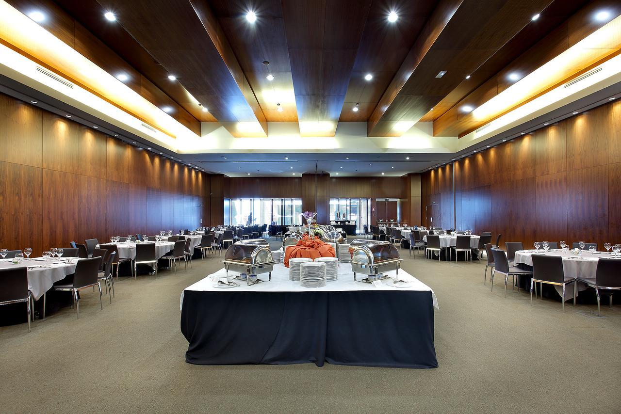 Eurostars Madrid Tower Hotell Exteriör bild The photo shows a spacious banquet hall or dining area with a modern design. The room features wooden walls and a high ceiling with lighting that creates a warm ambiance. In the center, there is a large table draped in black cloth, adorned with food 