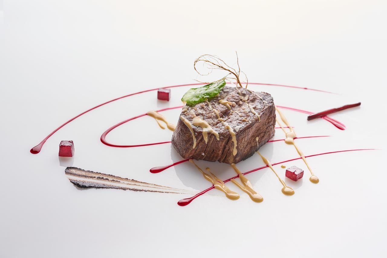 Eurostars Madrid Tower Hotell Exteriör bild The photo features a beautifully plated dish that showcases a piece of meat, likely a steak, at the center. The meat is glazed with a sauce and garnished with a thin piece of green herb. Surrounding the meat are artistic drizzles of different sauces,