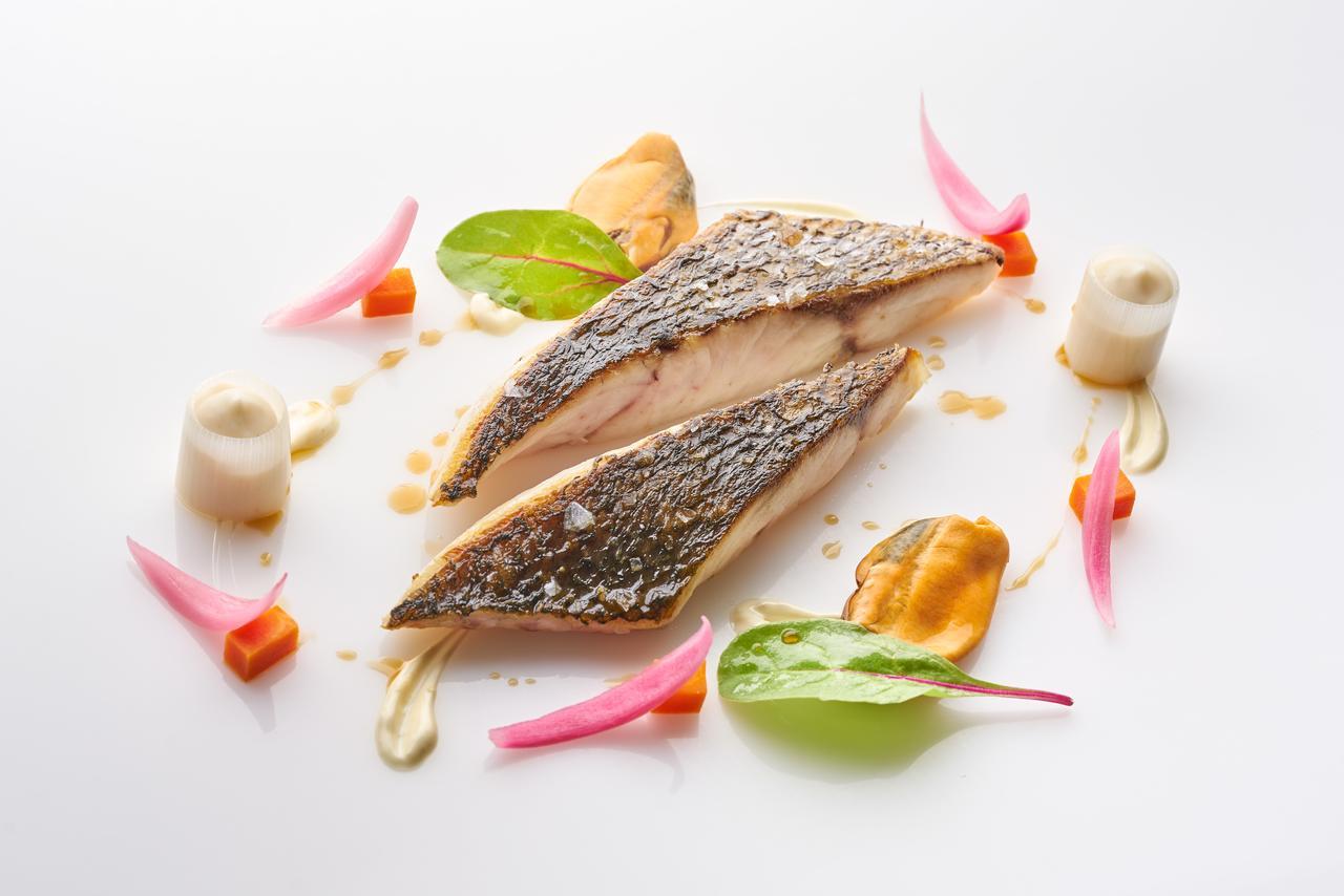 Eurostars Madrid Tower Hotell Exteriör bild The image depicts a beautifully plated dish featuring two pieces of fish fillet, likely a type of white fish, arranged artfully on a white plate. The fish has a crispy skin and is cooked to a tender texture. Surrounding the fish are various garnishes