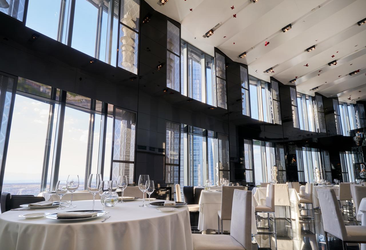 Eurostars Madrid Tower Hotell Exteriör bild The photo depicts an elegant restaurant interior characterized by sleek, modern design. It features large floor-to-ceiling windows that allow abundant natural light to fill the space and provide a panoramic view of the outside. The dining area includ