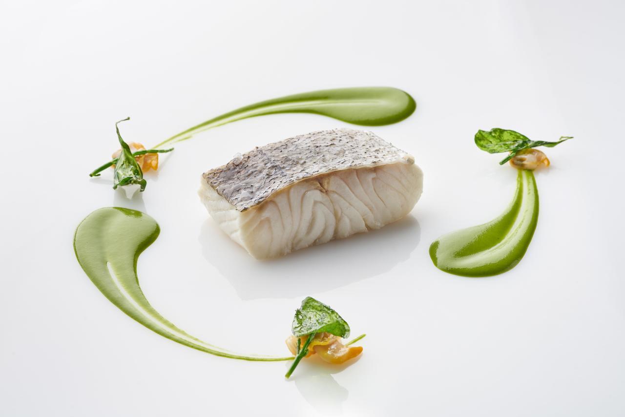 Eurostars Madrid Tower Hotell Exteriör bild The photo shows a beautifully presented dish featuring a piece of fish, likely a white fish, with a prominent skin side on top. It is surrounded by artistic garnishes, including vibrant green sauces and small sprigs of herbs. The composition is elega