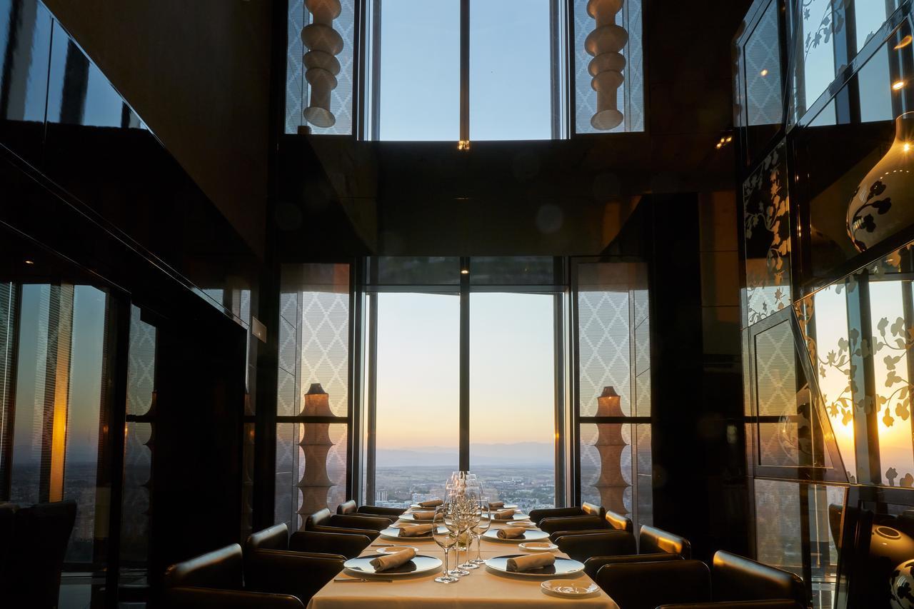 Eurostars Madrid Tower Hotell Exteriör bild The photo shows an elegantly set dining table in a restaurant with large glass windows. The view from the windows reveals a sunset, casting warm colors over the landscape. The table is tastefully arranged with plates and glassware, suggesting a fine 