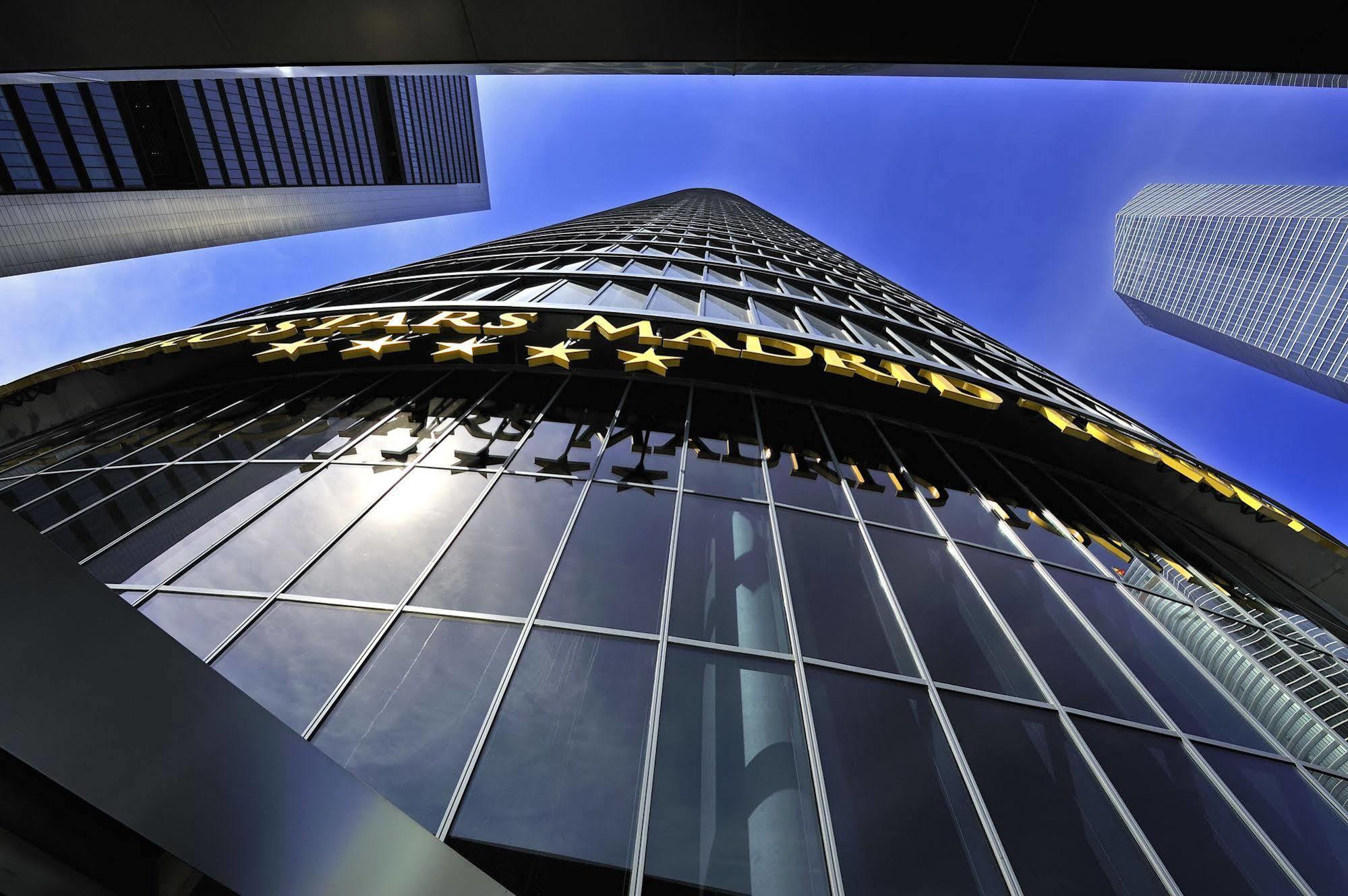Eurostars Madrid Tower Hotell Exteriör bild The photo shows a tall modern building reaching towards the sky. The perspective is from the ground looking upward, highlighting the building's height and glass facade. The building features a large sign that reads "MADRID" in bright yellow letters, 